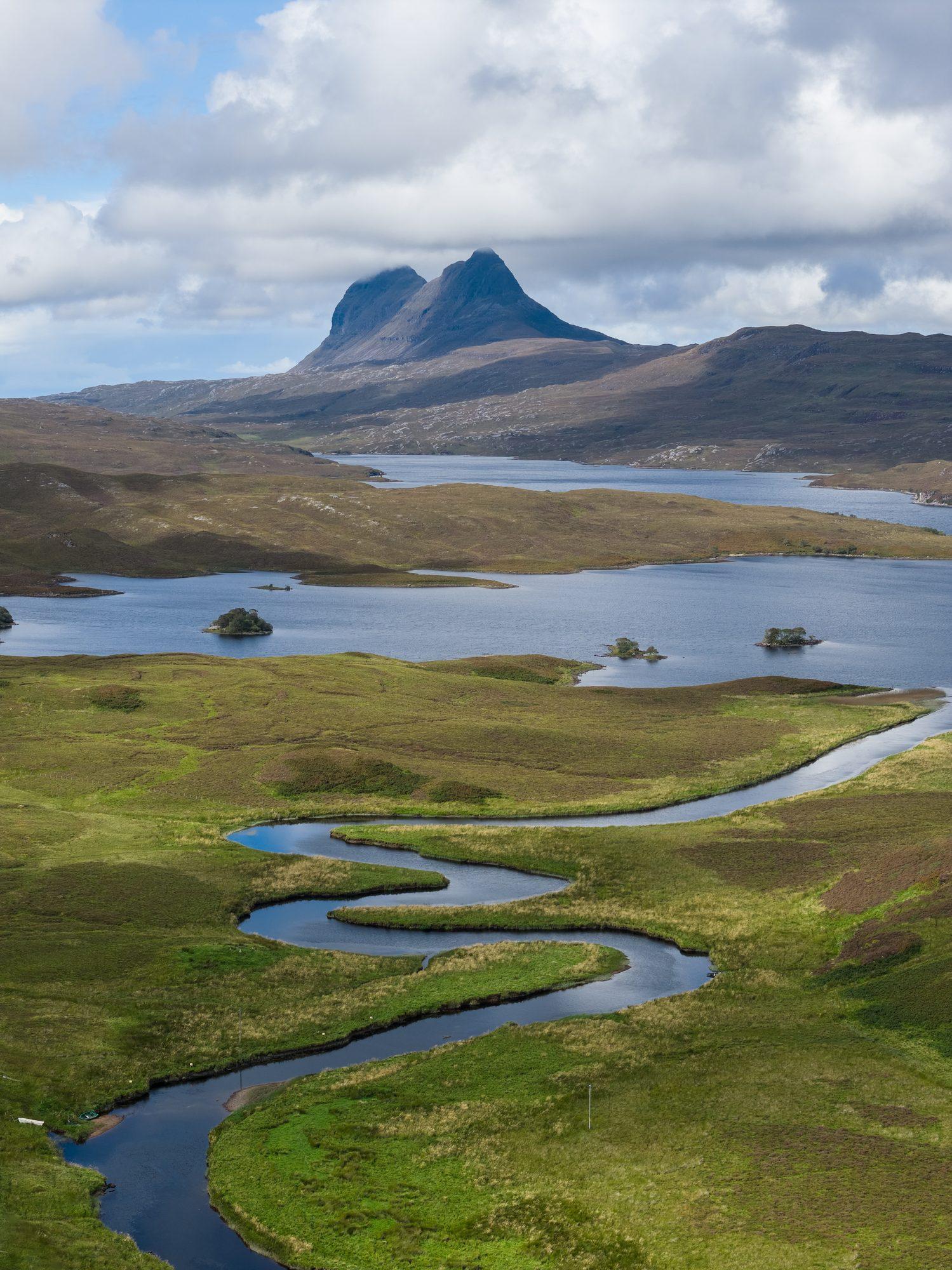 Aerial view of rivers winding through Highland moorland below a peak