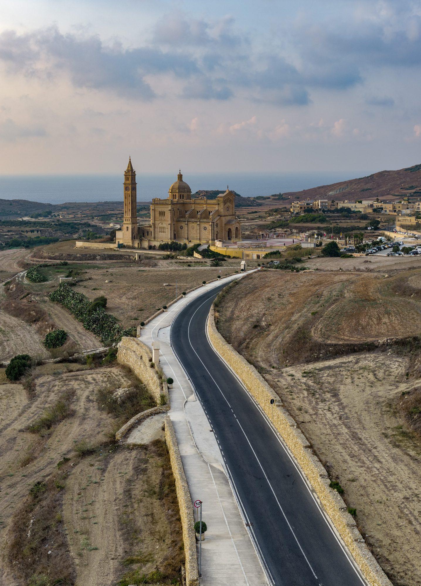 Aerial view of a coastal road curving past a clifftop tower